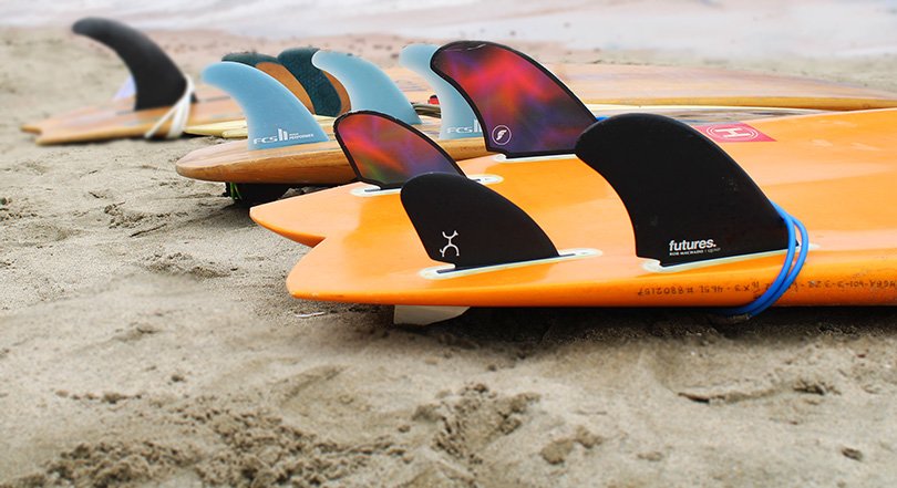 multiple surfboard fins laying out on a sandy beach