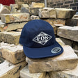 A navy blue 5-panel cap with a white embroidered 'SURF EOS SHOP' logo on the front, resting on a stack of rustic bricks.