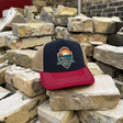 A trucker hat with a navy front panel, tan mesh back, and dark red brim sits on a pile of stacked bricks. The front panel features a colorful 'ECO SURF SHOP' logo.